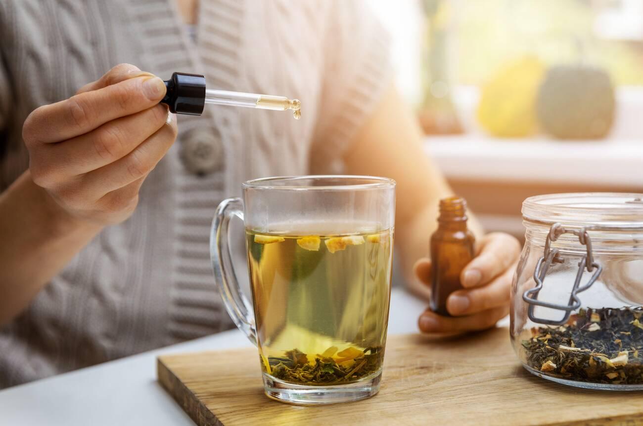 woman adding drop of cbd oil in cup of tea