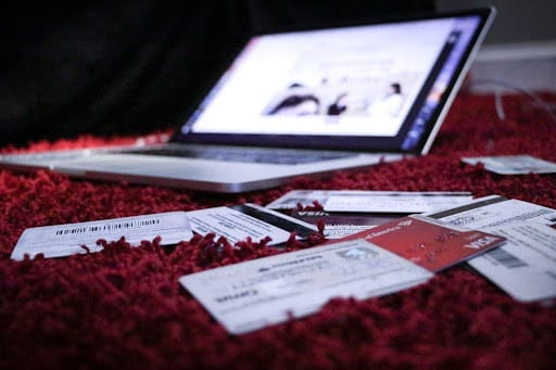 A laptop on the floor surrounded by credit cards and various bills to be paid.