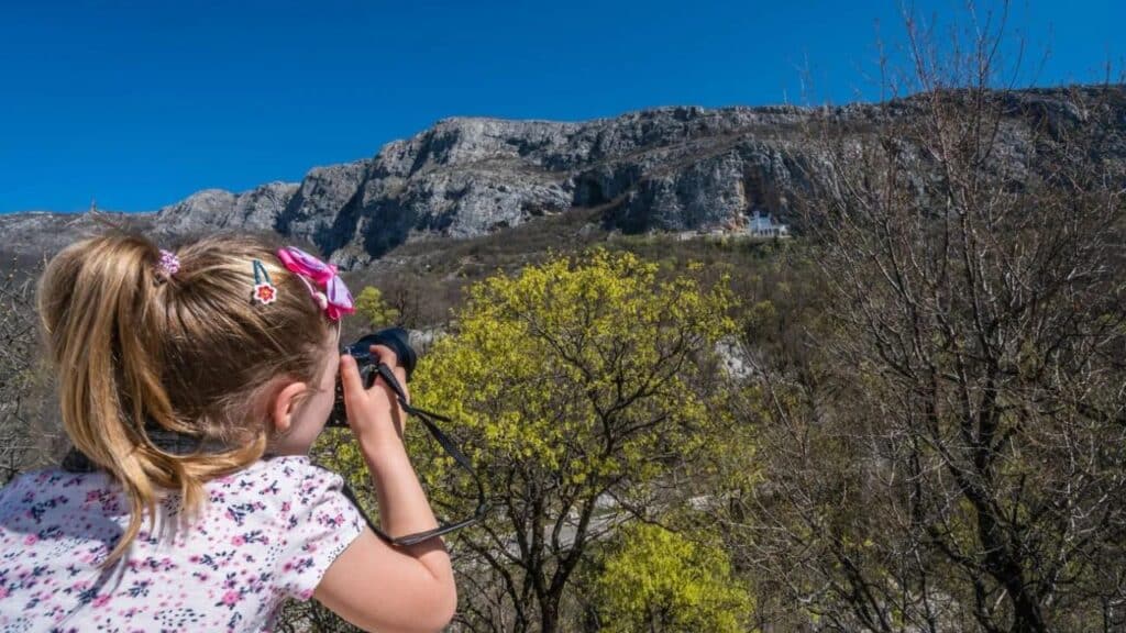 Young Caucasian girl taking pictures of the famous landmark Ostrog Orthodox monastery in Montenegro
