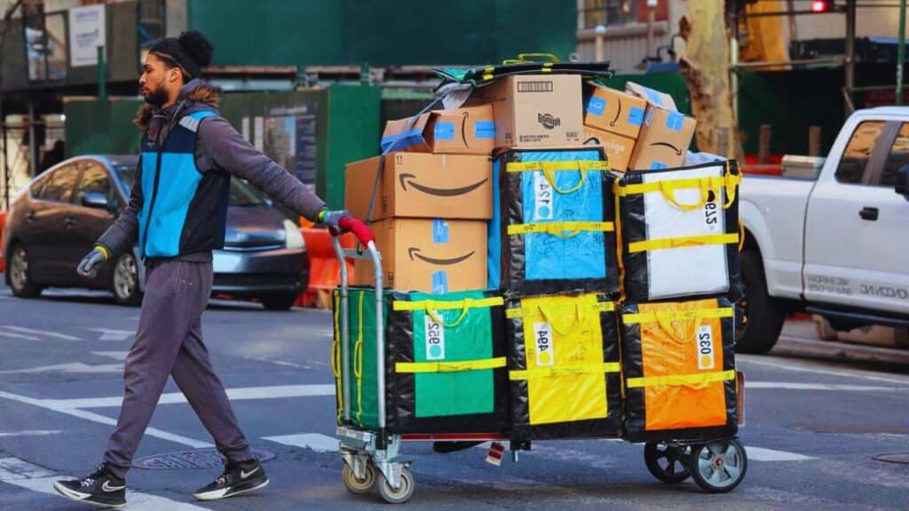 Delivery worker with a hand truck full of packages walks across the street, New York, NYC.