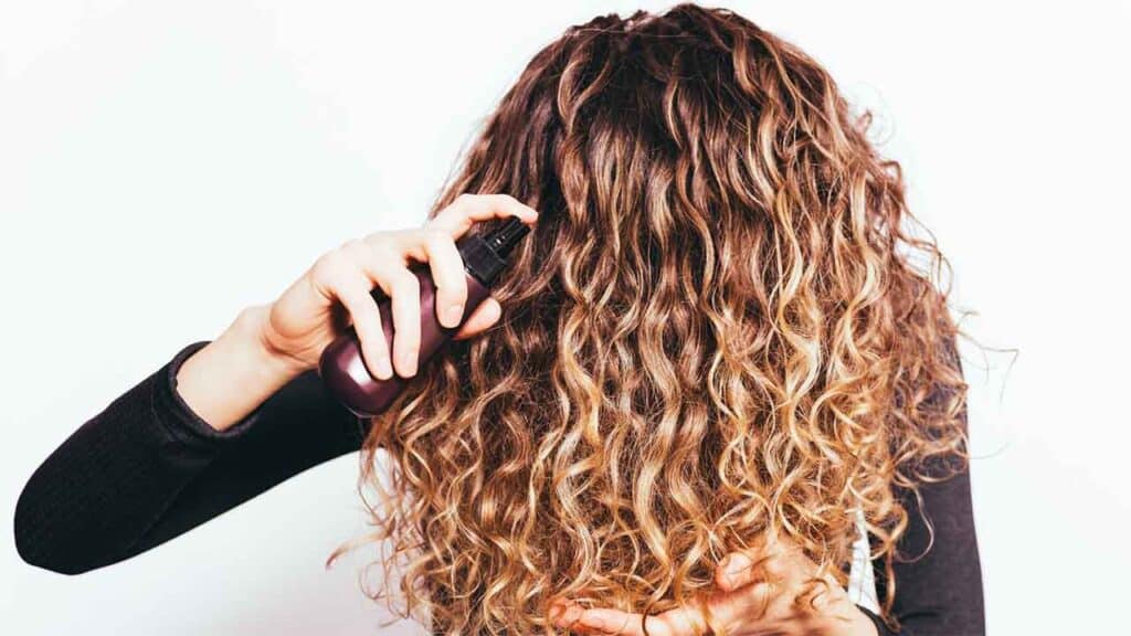 Person spraying product on curly hair.