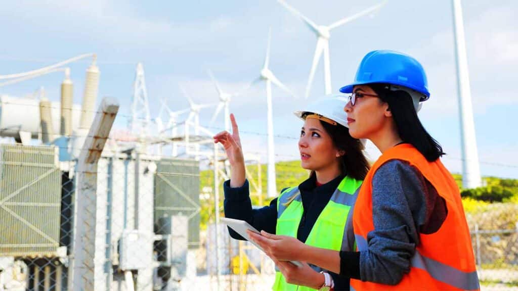 Two engineers in safety gear inspecting a wind farm with turbines in the background
