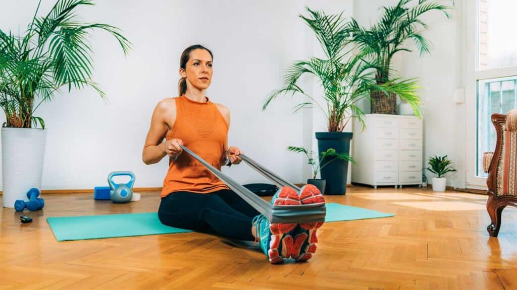 Woman doing seated resistance band row exercise at home.