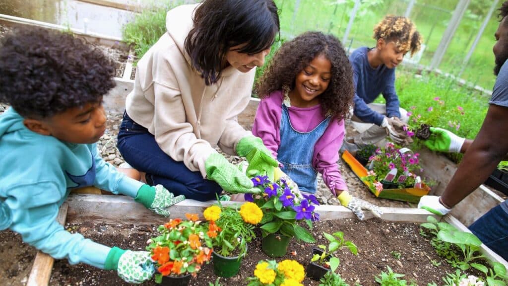 Family working together in a garden, planting flowers. A woman and three children.