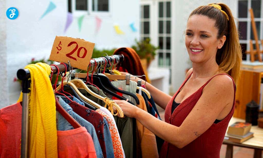 A woman is browsing through clothes on a rack at an outdoor market